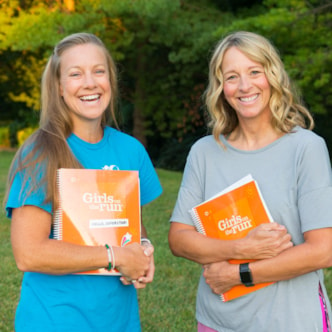 Two smiling Girls on the Run coaches holding curriculum books